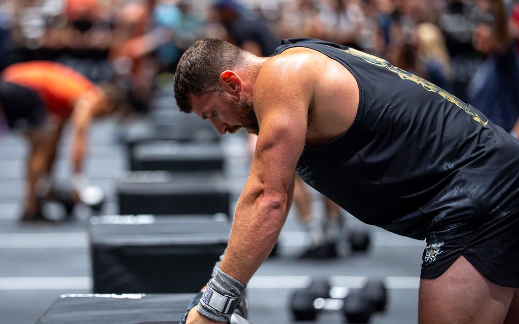 Kyle bent over with one hand on a plyo box, catching his breath between sets on the competition floor