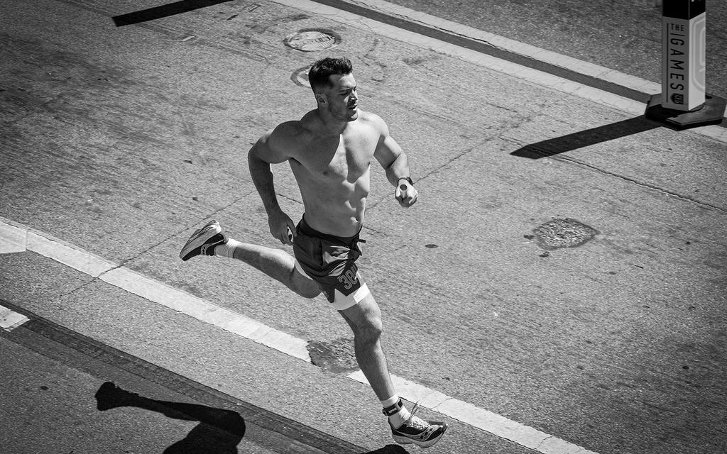 Black-and-white overhead shot of a shirtless athlete running on a city street during the CrossFit Games