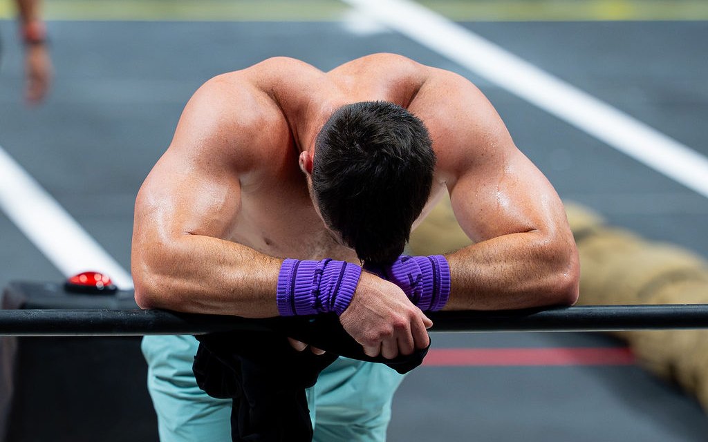 An athlete slumped forward over a bar between events at the CrossFit Games, head down